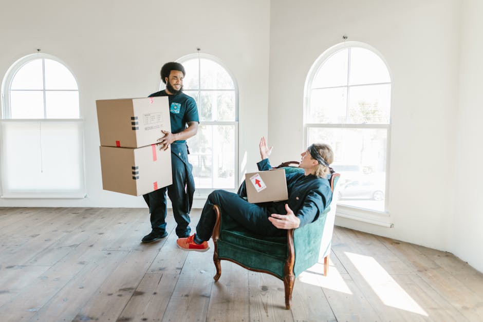 A professional mover from France Removals is carefully lifting a green upholstered sofa with tufted buttons and wooden legs through an interior doorway during a home relocation process. The mover is w
